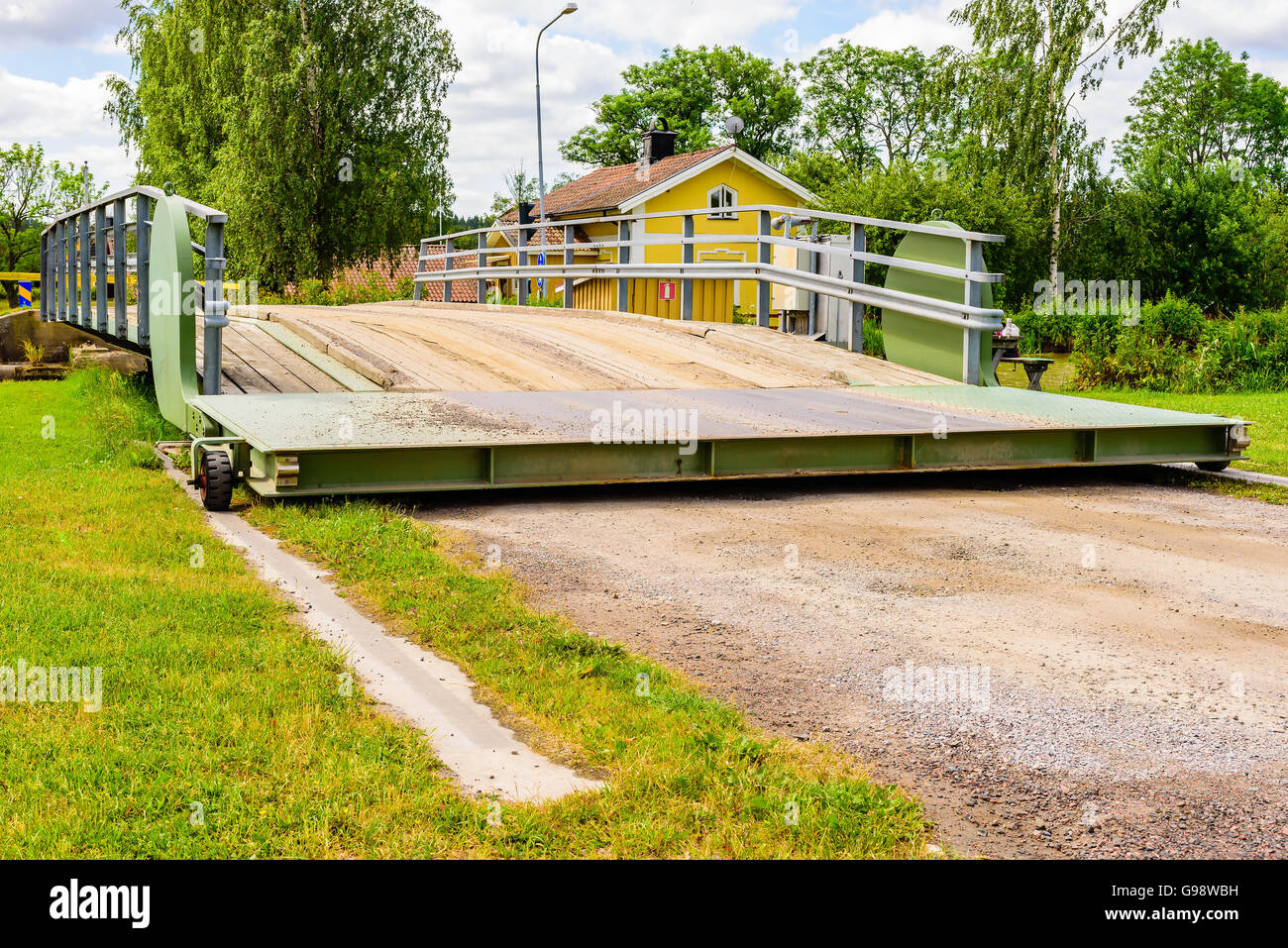 Small rolling bridge opening. It has just lifted from the ground and started its roll over the track. Canal and house in backgro Stock Photo