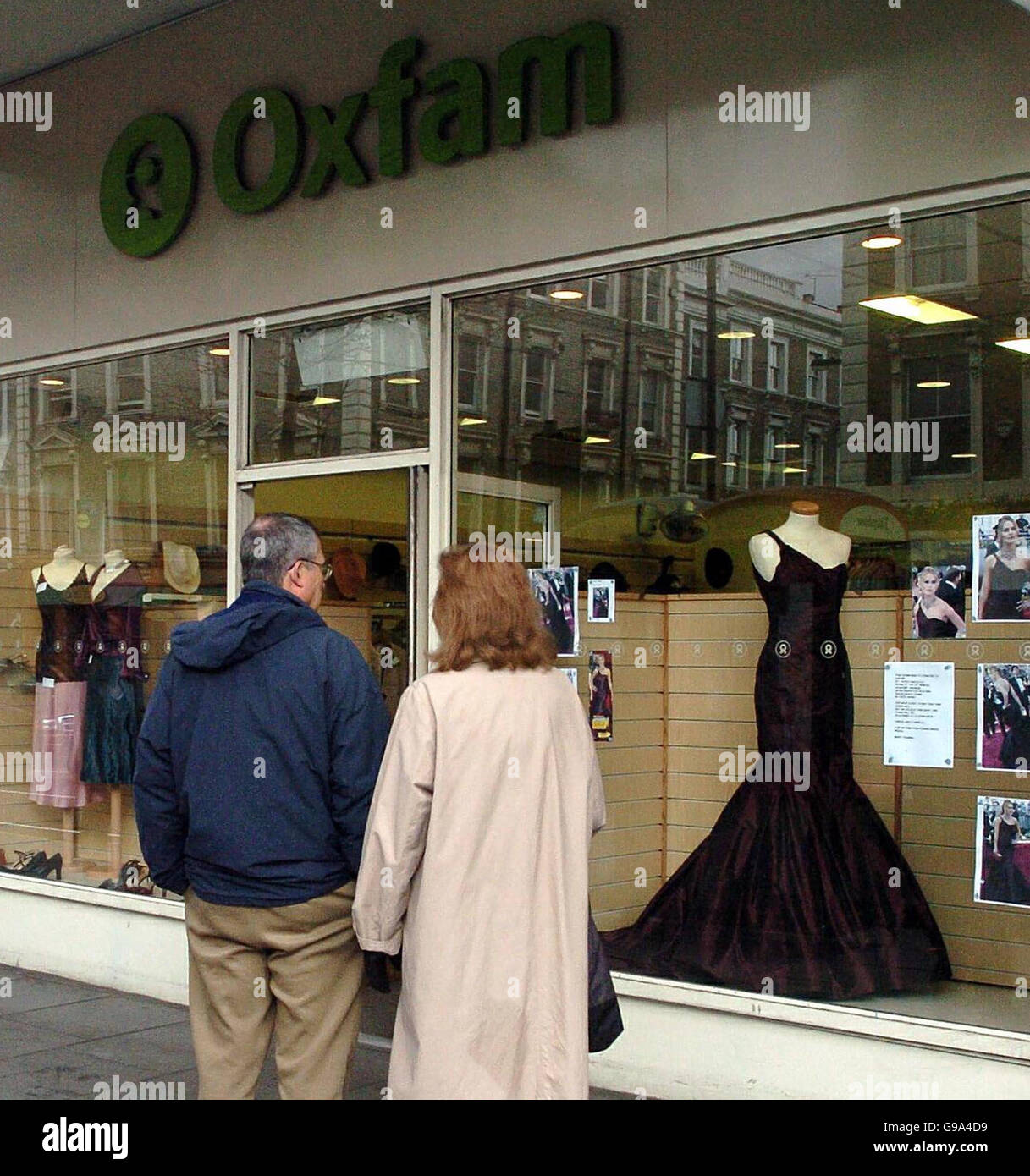 Passers-by gaze at the dress worn by actress Keira Knightley to the Oscars displayed in the window of an Oxfam shop in London's Notting Hill, Friday April 7, 2006. Knightley is donating the silk off-the-shoulder dress she wore at the Oscars to Oxfam. The deep-claret taffeta gown, custom made by Vera Wang, will be auctioned to the highest bidder on eBay. All proceeds will support Oxfam's work to counter the humanitarian emergency in drought-hit East Africa. See PA story SHOWBIZ Knightley. Stock Photo
