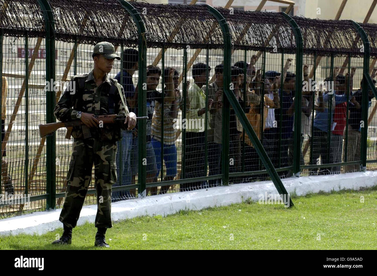 Cricket fans are kept behind barbed wire and fencing as an armed officer keeps guard during an England nets session at the Keenan Stadium, Jamshedpur, India. Stock Photo