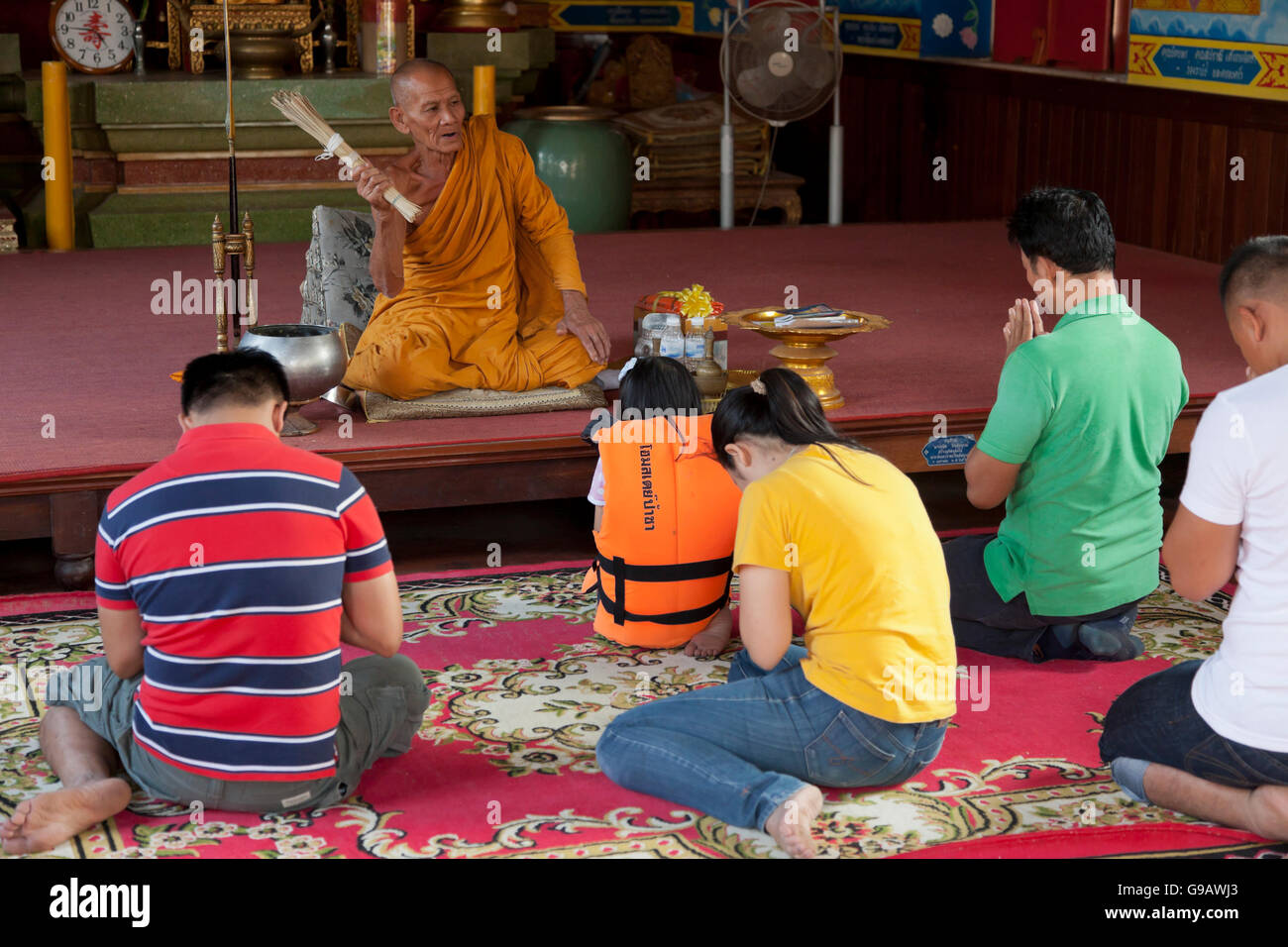 A monk using a bundle of reeds to sprinkle holy water on a group of Thais praying in the main temple hall of Wat Phummarin in Ma Stock Photo