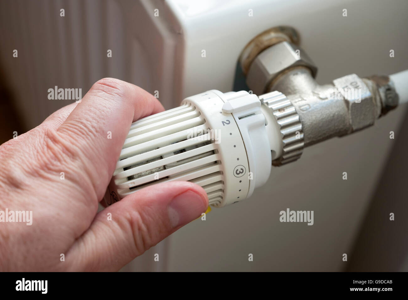 Man turning down thermostat on gas powered central heating radiator to save energy Stock Photo