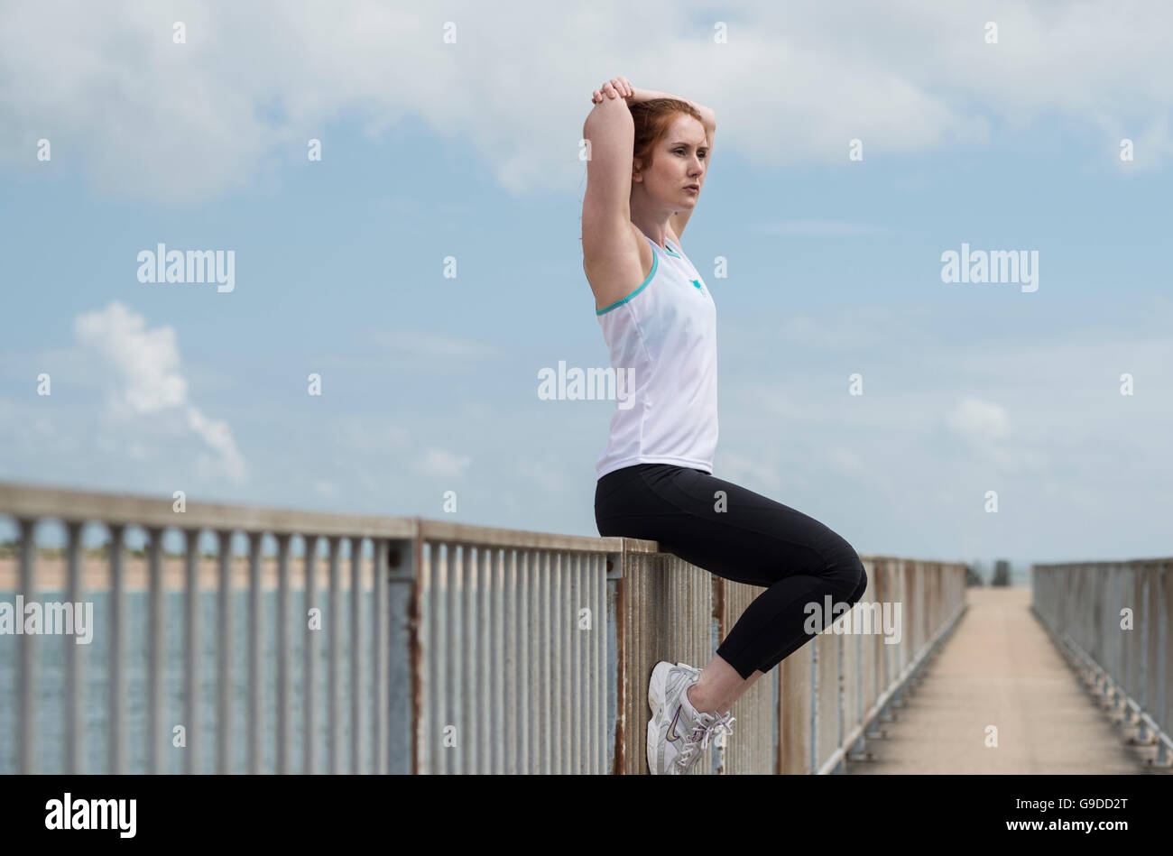 woman sitting on railings doing an arm stretch, outdoor exercise Stock Photo