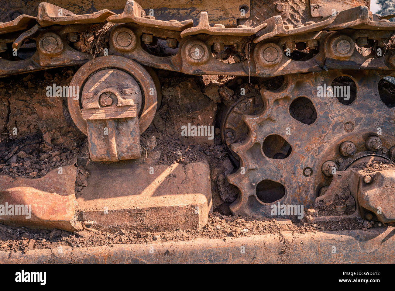 Rusty and dirt covered mechanical caterpillar track with aged cogs and wheels. Stock Photo