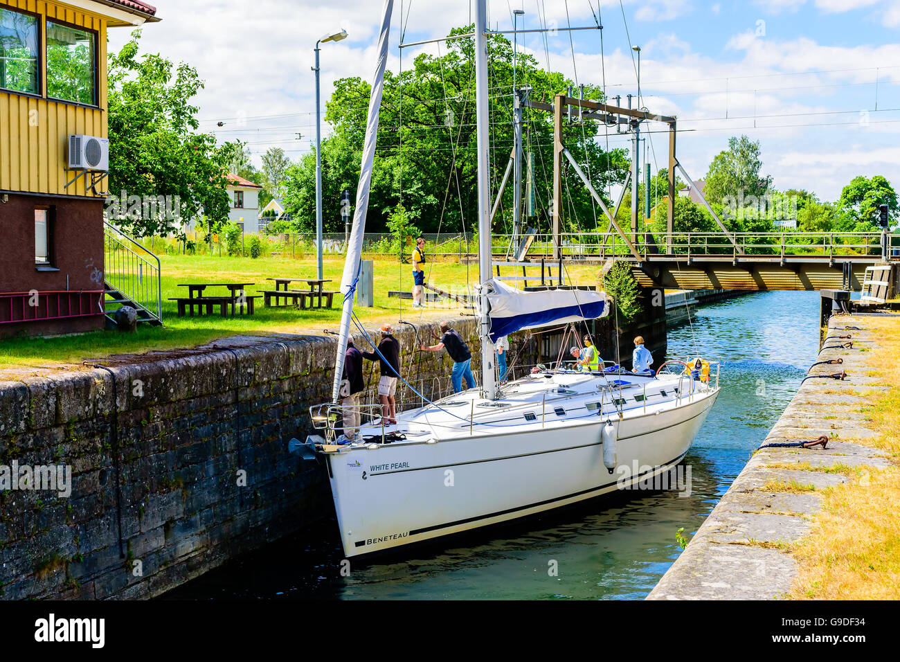 Norsholm, Sweden - June 20, 2016: Beneteau sailboat with crew passing a canal lock. Crew is holding on to ropes and pull to keep Stock Photo