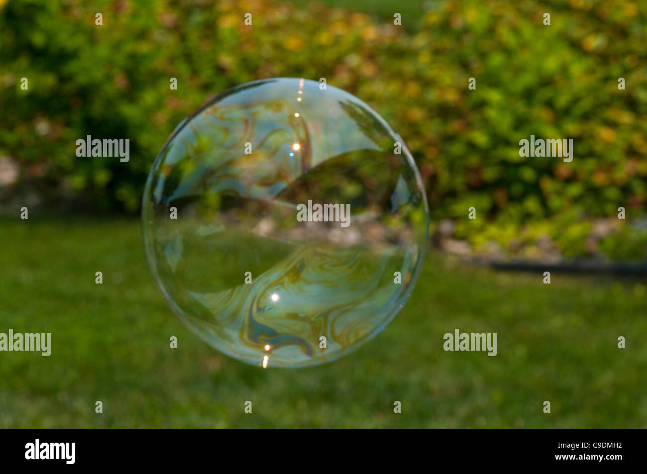 A soap bubble floats through the air in front of grass and trees