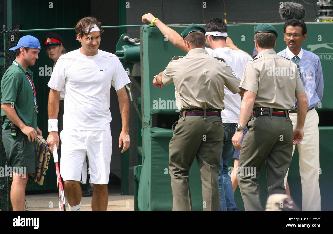 Roger Federer watches as a member of Real Fathers 4 Justice, a breakaway group from Fathers 4 Justice, is led off Centre Court at Wimbledon during the men's singles quarter-final match between Switzerland's Roger Federer and Croatia's Mario Ancic. Stock Photo