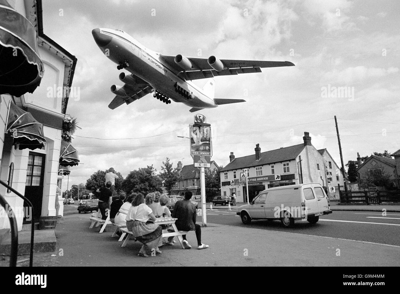 Customers enjoying a quiet lunchtime drink in Farnborough look skywards as a giant aircraft, the Soviet AN-124 transport plane, the biggest aircraft in the world, flies in for the Farnborough Air Show. Stock Photo