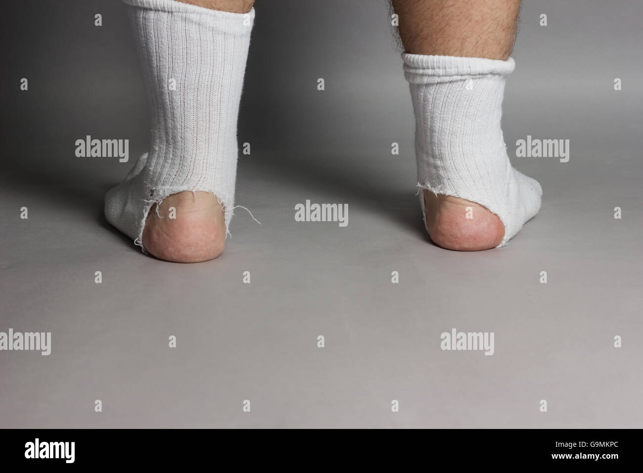 back of standing feet with white socks and a big hole in front of grey background Stock Photo