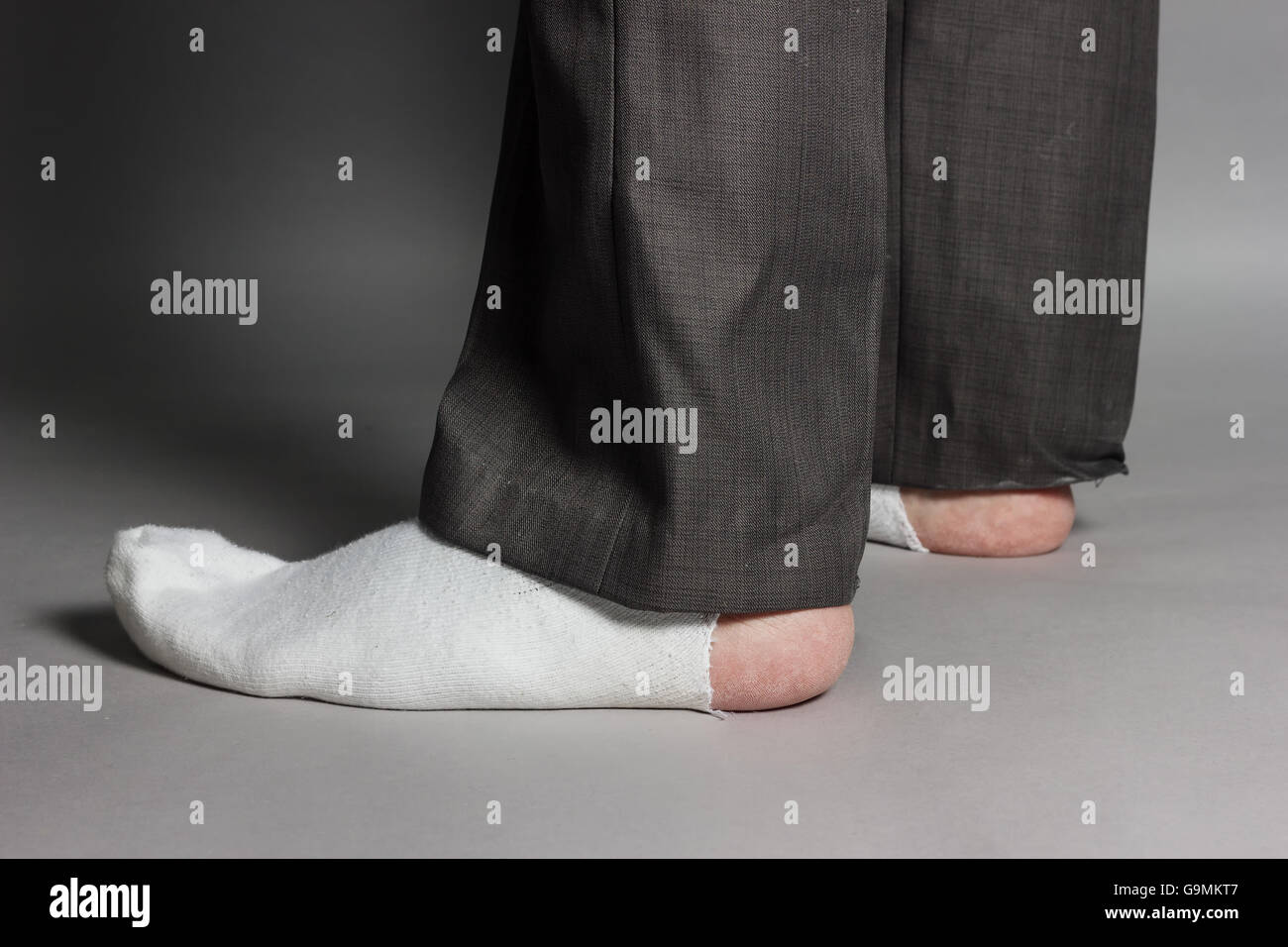 sideways standing feet with white socks and a big hole in front of grey background Stock Photo