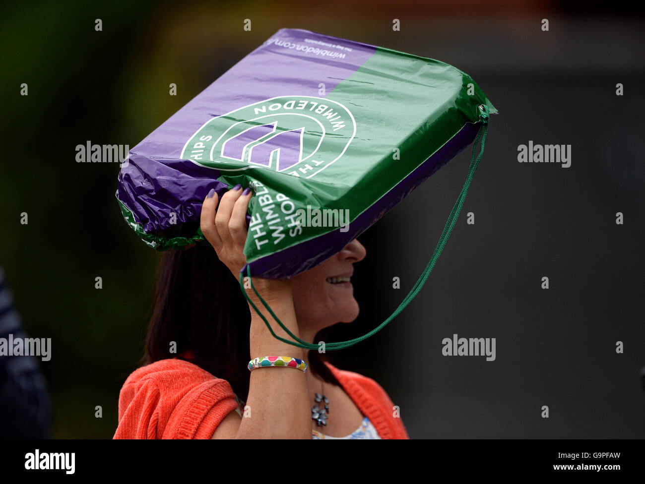 A spectator uses a Wimbledon branded plastic bag to shelter from the rain on day Five of the Wimbledon Championships at the All England Lawn Tennis and Croquet Club, Wimbledon. Stock Photo