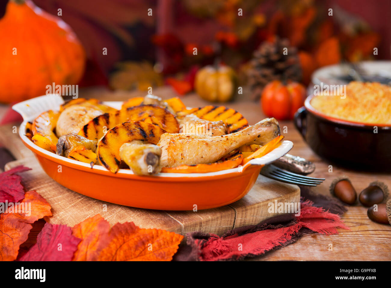 A casserole with oven roasted chicken and grilled pumpkin on a rustic table with autumn decorations. Stock Photo