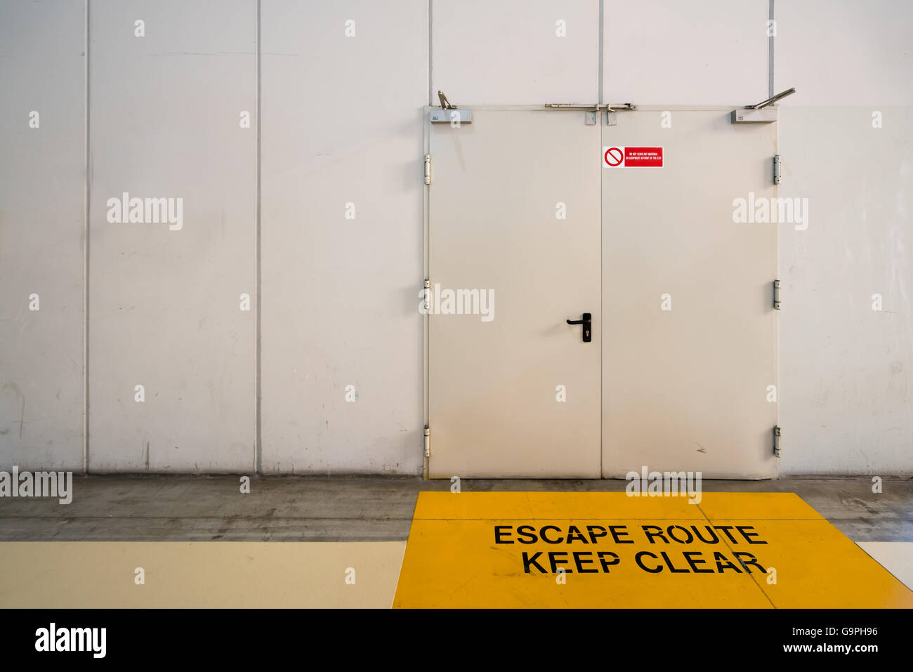 Emergency exit door with keep clear warning message on floor, copy space on wall Stock Photo
