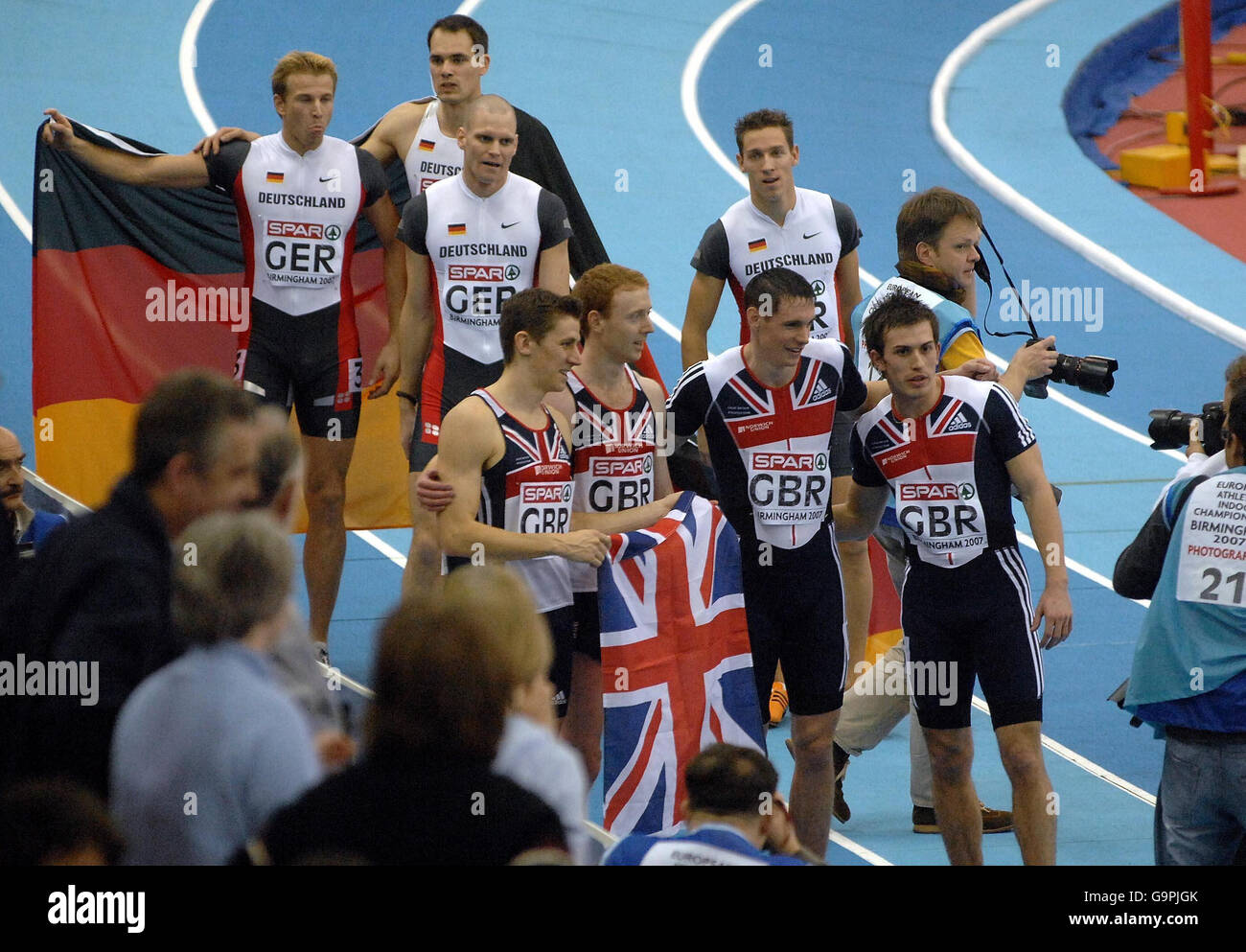 The Great Britain relay team Robert Tobin, Dale Garland, Phillip Taylor and Steven Green are followed around the track by the German relay team as confusion reigns over a pushing incedent during the 4x400m relay in the European Athletics Indoor Championships at the National Indoor Arena, Birmingham. Stock Photo