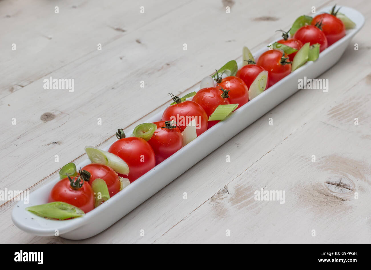 White elongated dish filled with cherry tomatoes, spring onions and pepper Stock Photo