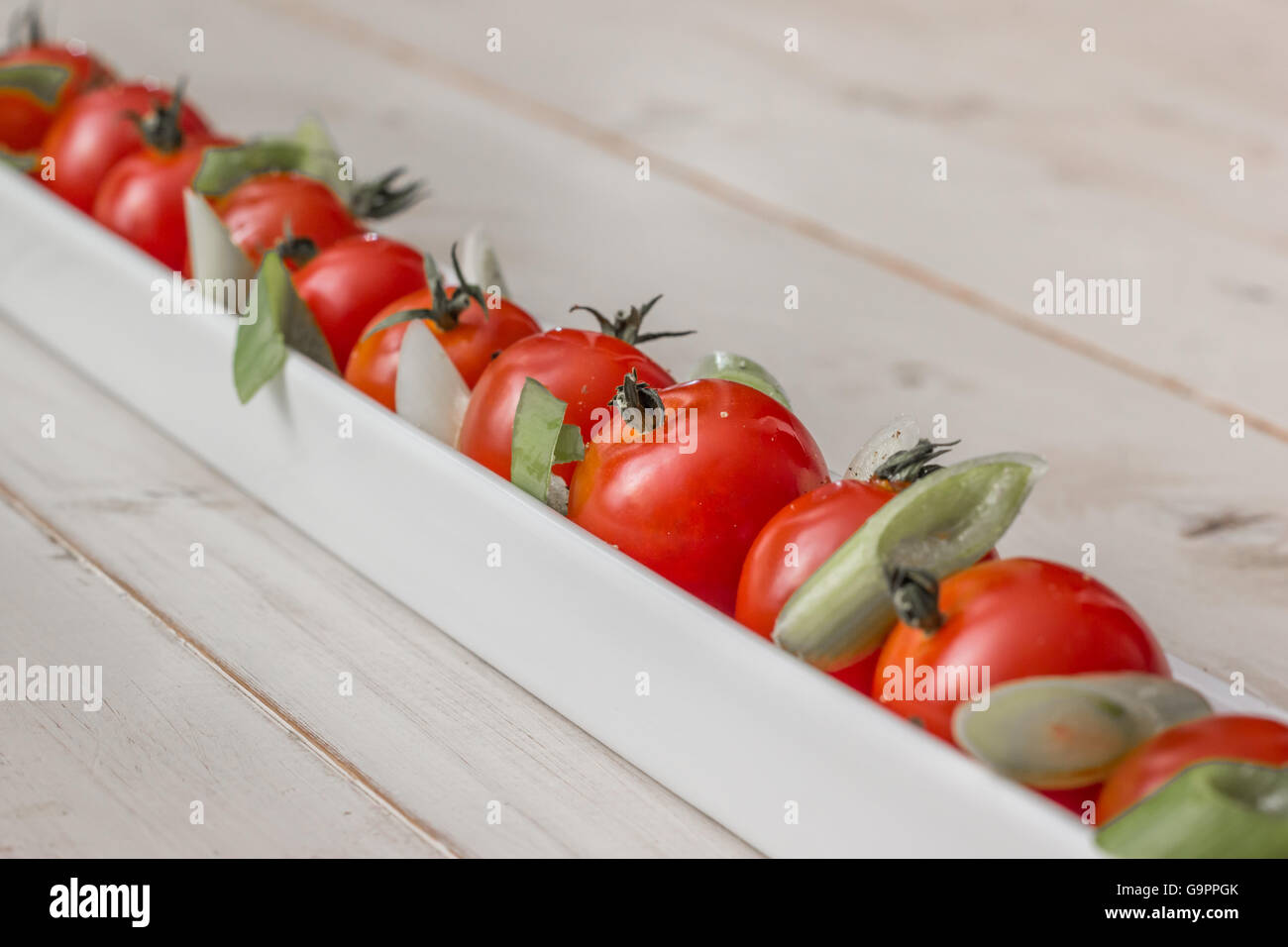 White elongated dish filled with cherry tomatoes, spring onions and pepper Stock Photo