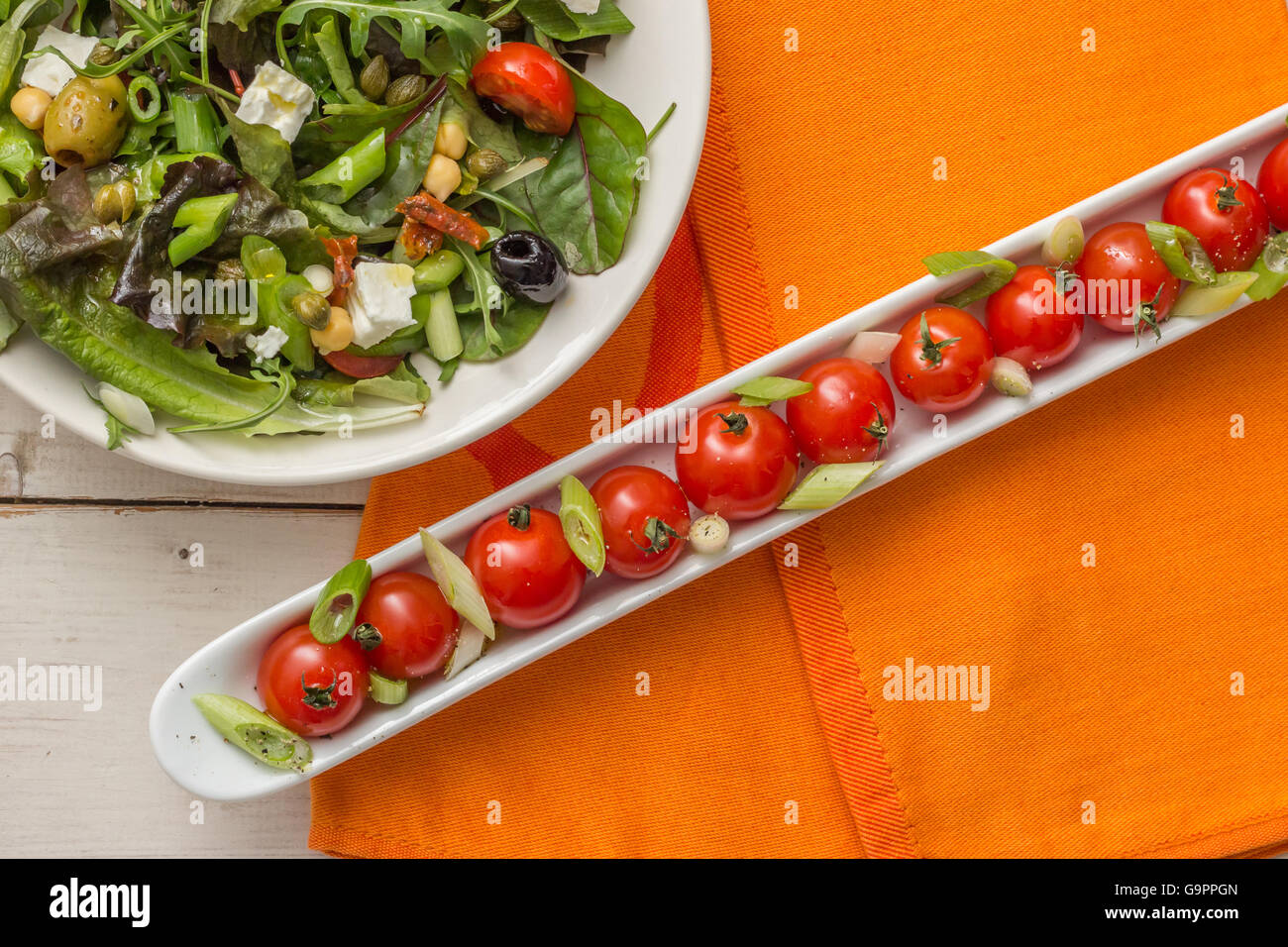 Long dish with cherry tomatoes and a green salad on a white wooden table Stock Photo