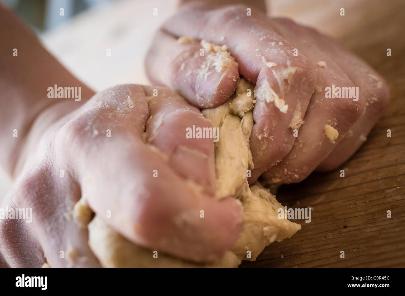Close-up of two strong hands of a baker that are manually kneading dough on a rough, wooden kitchen table Stock Photo