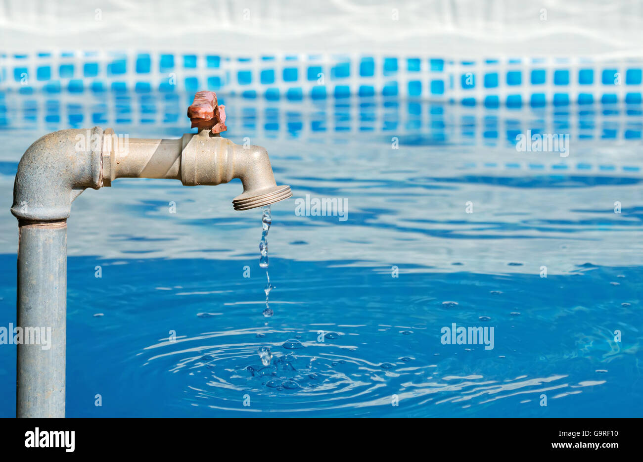 faucet dripping in a blue pool on a sunny day Stock Photo