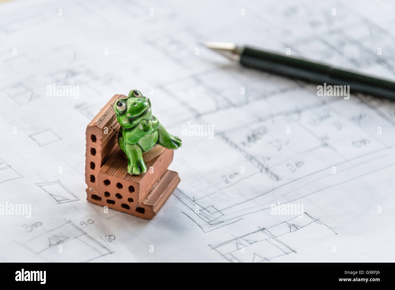 Toy frog sitting on a brick on architect sketches background Stock Photo