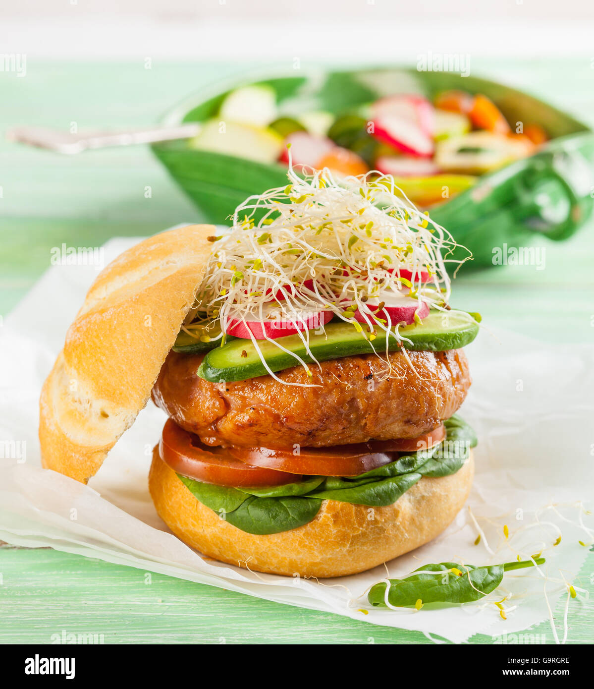 A delicious gourmet hamburger with fresh vegetables: tomato, spinach, pickles, radish and sprouts Stock Photo