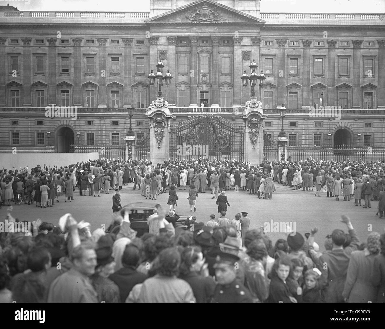 Londoners surge around the gates of Buckingham Palace as newly-engaged couple, Princess Elizabeth and her fiance Lieutenant Philip Mountbatten, acknowledge their cheers from the balcony. Stock Photo