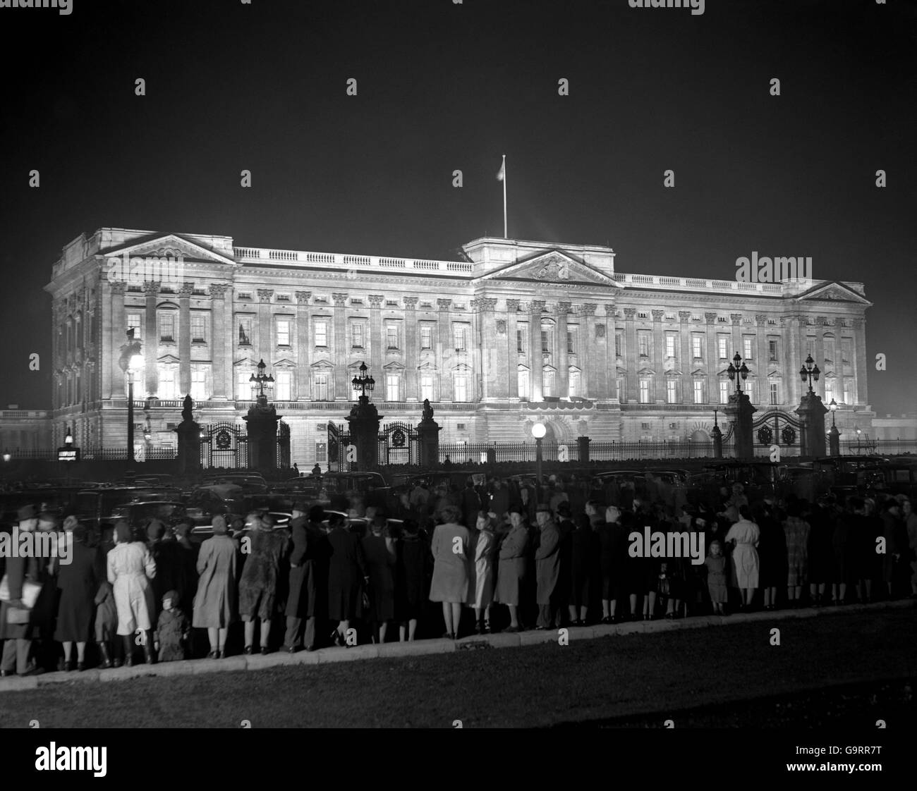 Buckingham Palace stands bathed in light against the night sky as people in hundreds surge to the railings for the Princess and her fiance this evening Stock Photo