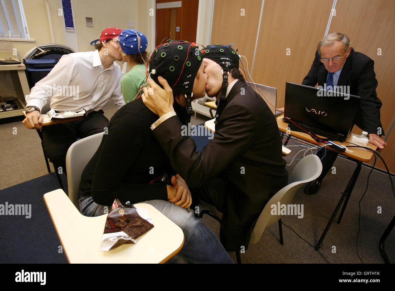 Study participants kissing while sensors measure the electrical activity of their brains as Cognitive Neuroscientist, Dr David Lewis looks on in the Middlesex University Human Performance Lab. Stock Photo