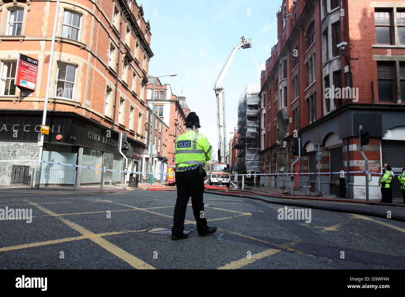 Manchester fire. A police officer looks on as firefighters tackle a