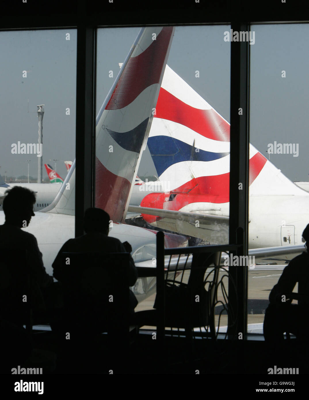 Passengers look out of a window at Heathrow Airport's Terminal 4 as a British Airways aircraft taxis towards the runway. Stock Photo