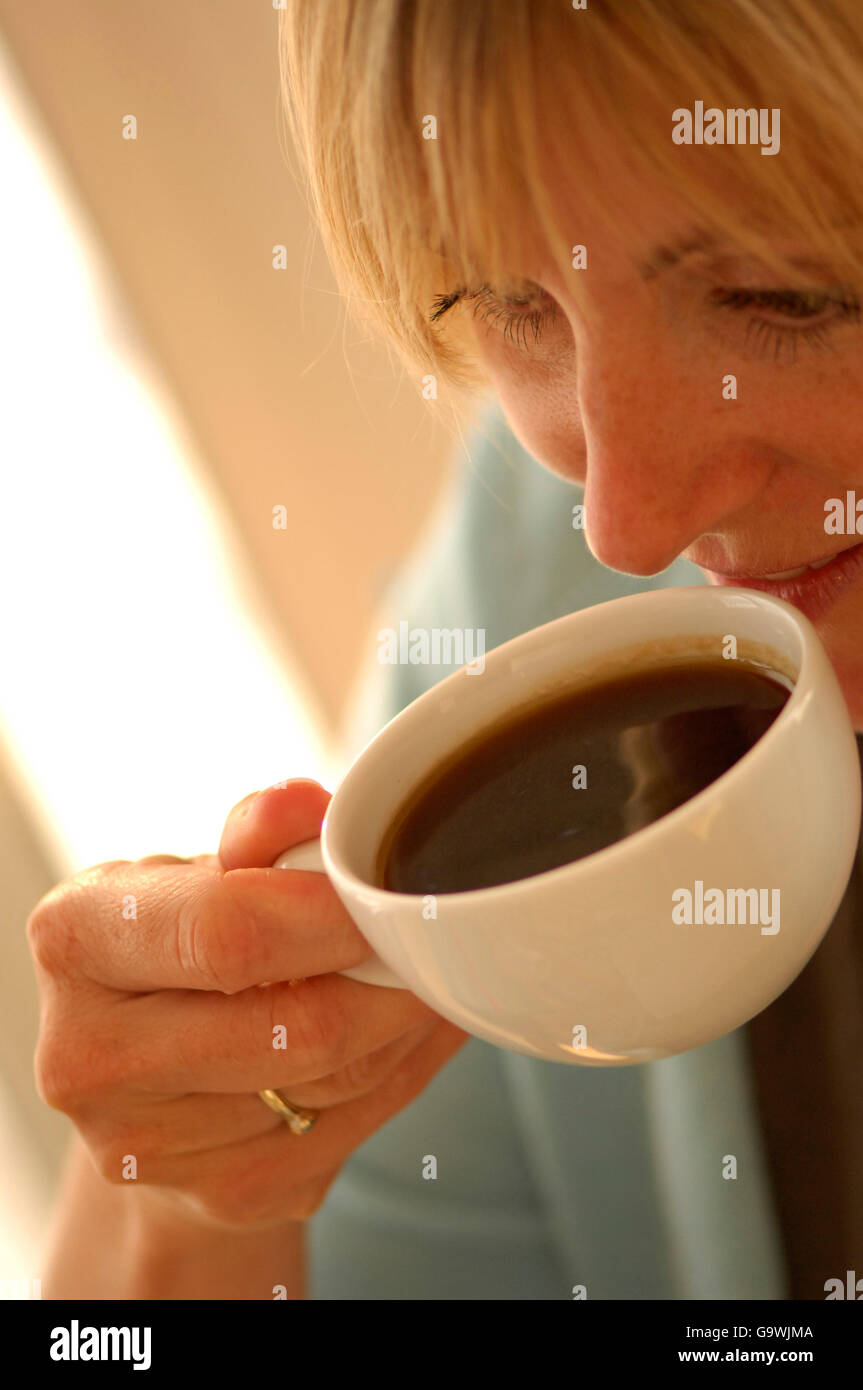 Beautiful blonde lady drinking morning coffee and reading the newspaper Stock Photo