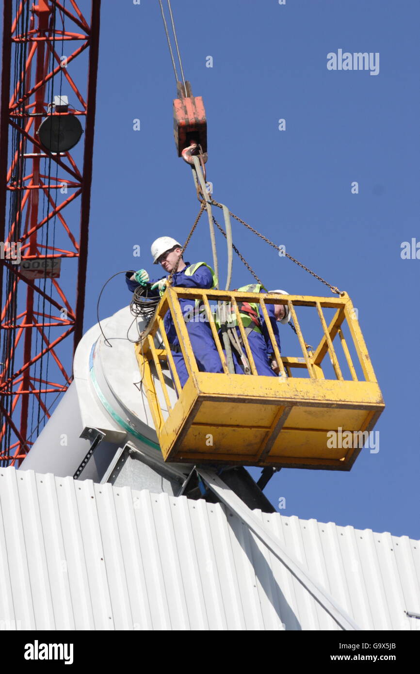 Two workmen access the roof of an industrial plant using a cradle lifted by a crane. Stock Photo