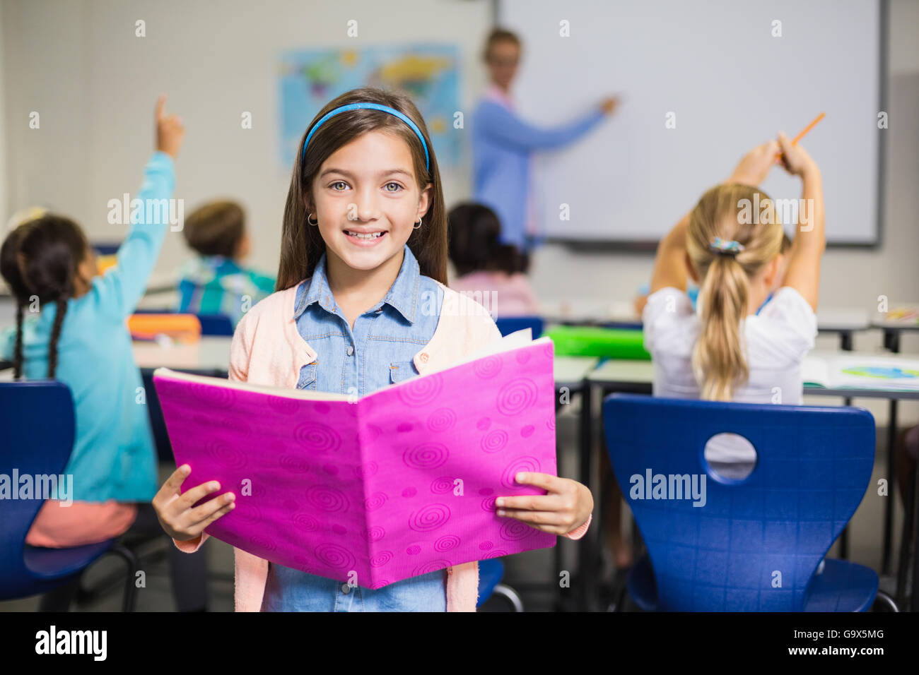 Portrait of schoolgirl standing with book in classroom Stock Photo - Alamy