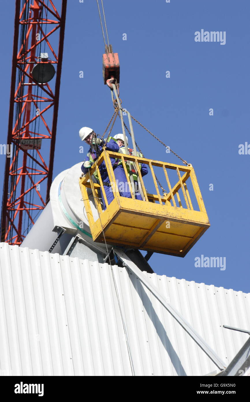 Two workmen access the roof of an industrial plant using a cradle lifted by a crane. Stock Photo