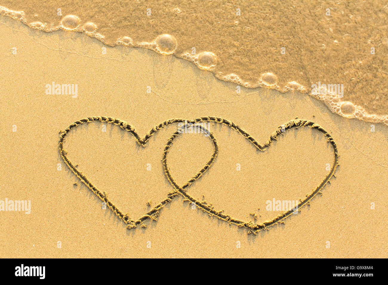 Couple of hearts drawn by hand on a sandy golden sea beach. Stock Photo