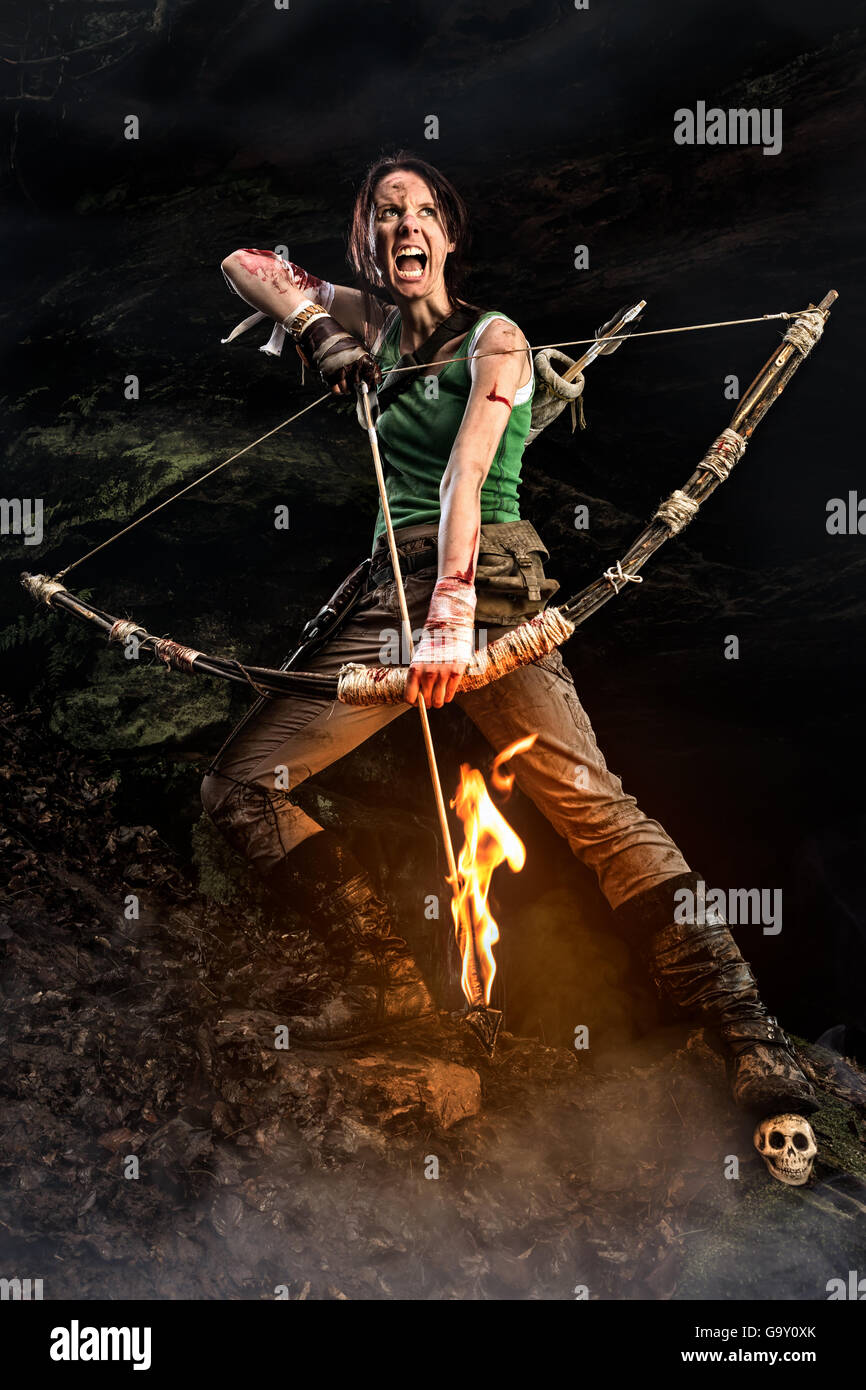 Rise of the Tomb Raider. screaming woman dressed up as Lara Croft holds a bow and pulls the bowstring with a burning arrow. Stock Photo