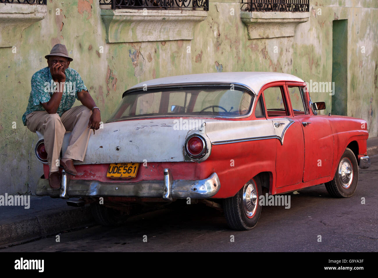 Cuban taxi driver sitting on a vintage taxi car, Santiago de Cuba, Province of Santiago de Cuba, Cuba Stock Photo