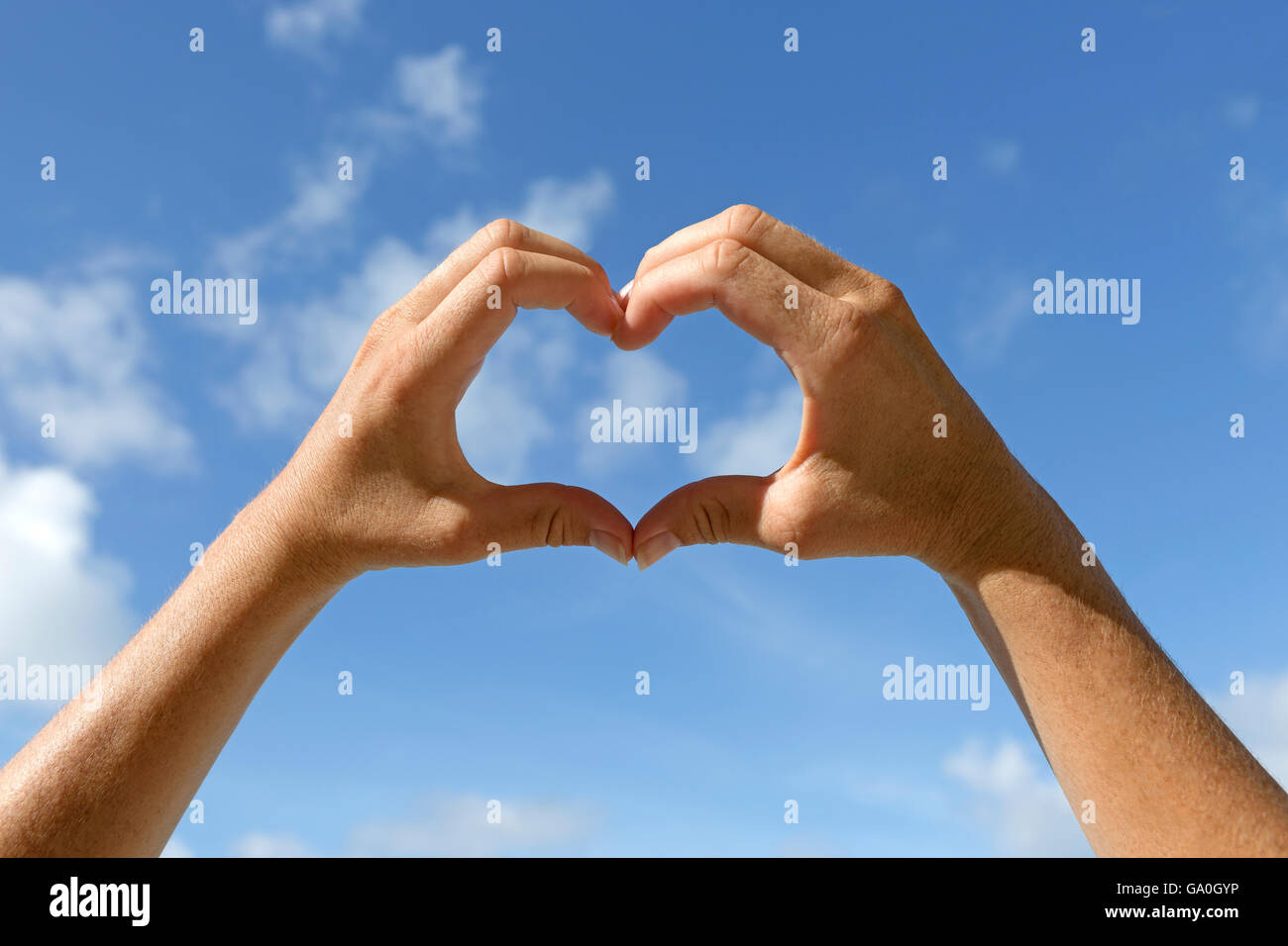 Female hands shows love sign in the air with blue sky Stock Photo
