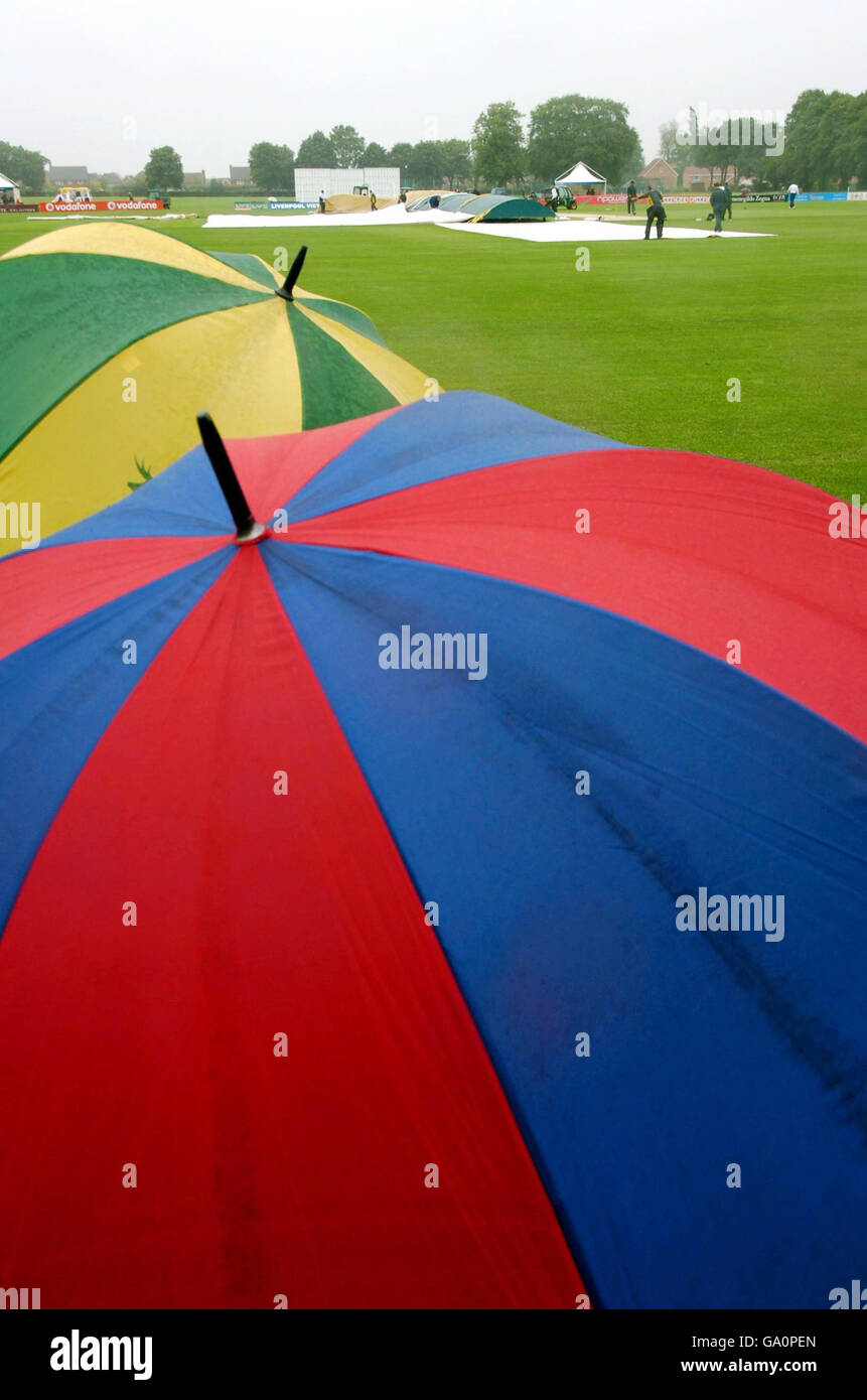 Fans watch from under their umbrella's as groundstaff replace the covers on the pitch before the start of the Liverpool Victoria County Championship Division Two match between Leicestershire and Nottinghamshire match at Oakham School. Stock Photo