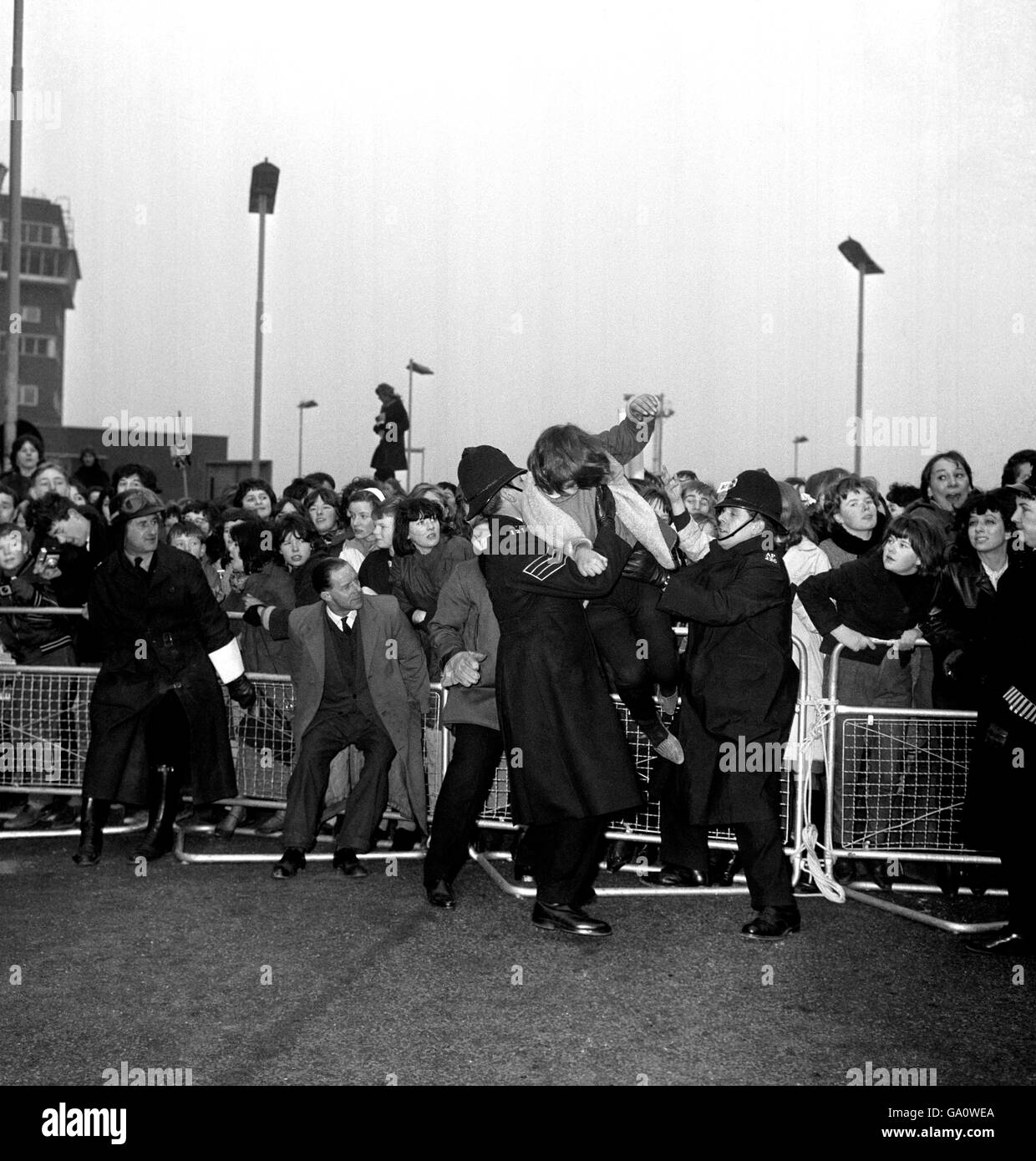 Policemen restrain an over enthusiastic barrier hopping fan as The Beatles arrive at London Airport from America. Stock Photo
