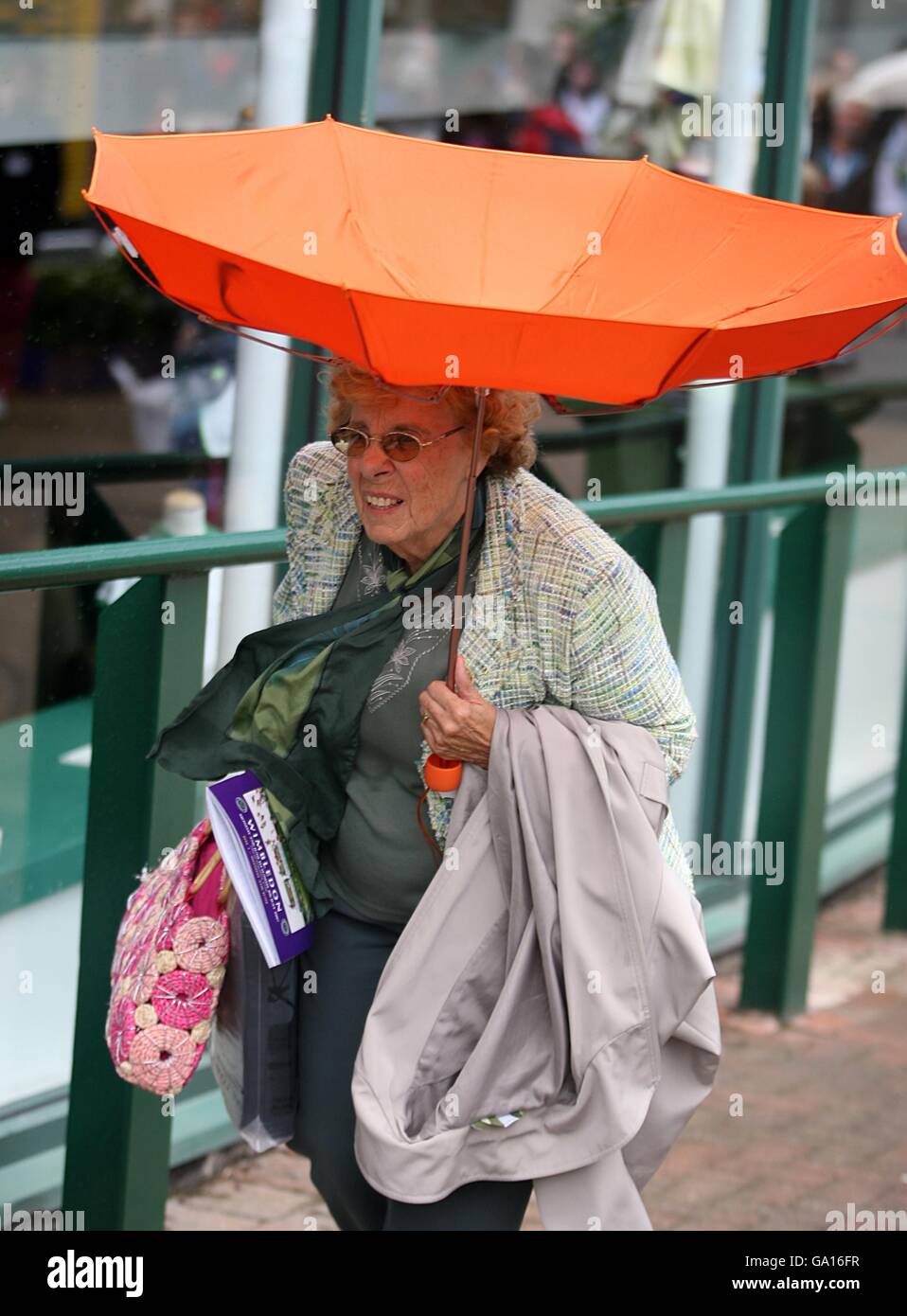 Tennis - Wimbledon Championships 2007 - Day One - All England Club. A Tennis fans walks on as her umbrella blows inside out Stock Photo