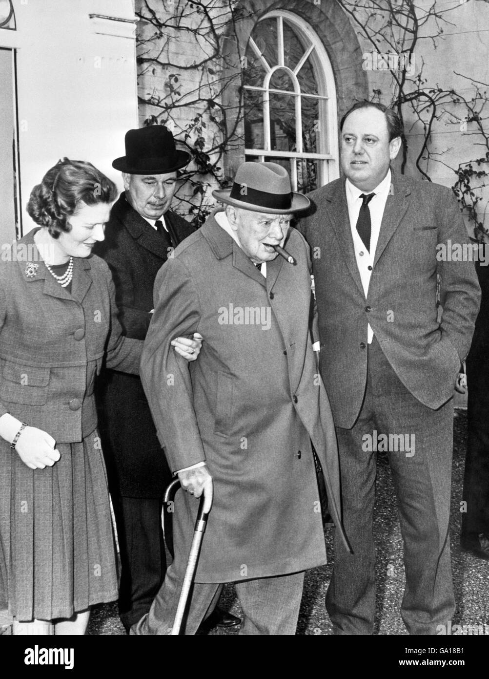 Sir Winston Churchill, the inevitable cigar between his lips, gets an affectionate helping hand from his daughter, Mary, and son-in-law Christopher Soames, as he leaves their Georgian home at Hamsell Manor, Eridge Green, near Tunbridge Wells. With Lady Churchill, he had been a guest at a family luncheon party to celebrate her 79th birthday. They had driven over from their home at Chartwell, Kent Stock Photo