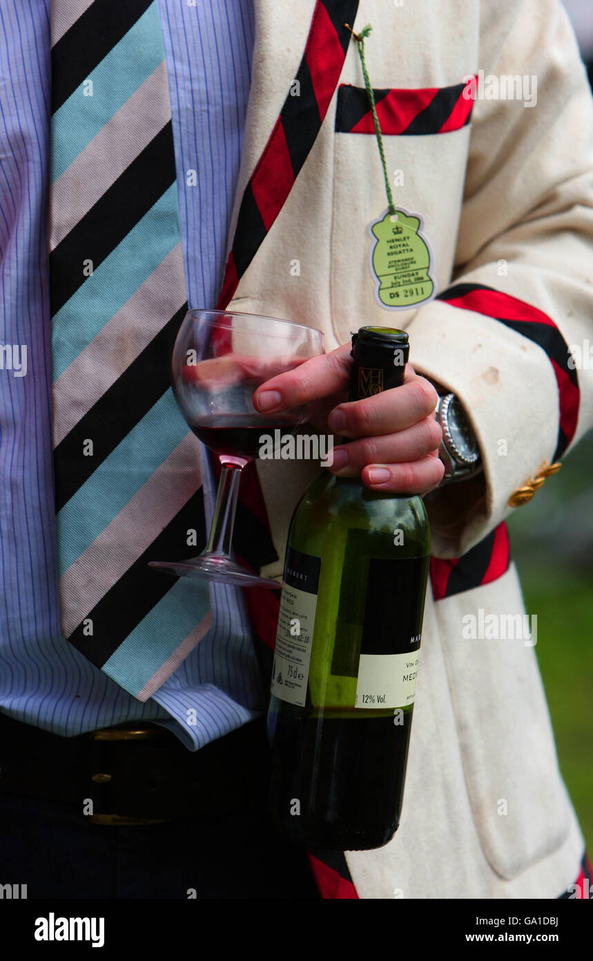 A man wearing a Jesus College Blazer holds a wine bottle and glass during the Final day of the Cambridge University May Bumps along the river Cam at Fen Ditton Cambridgeshire. Stock Photo