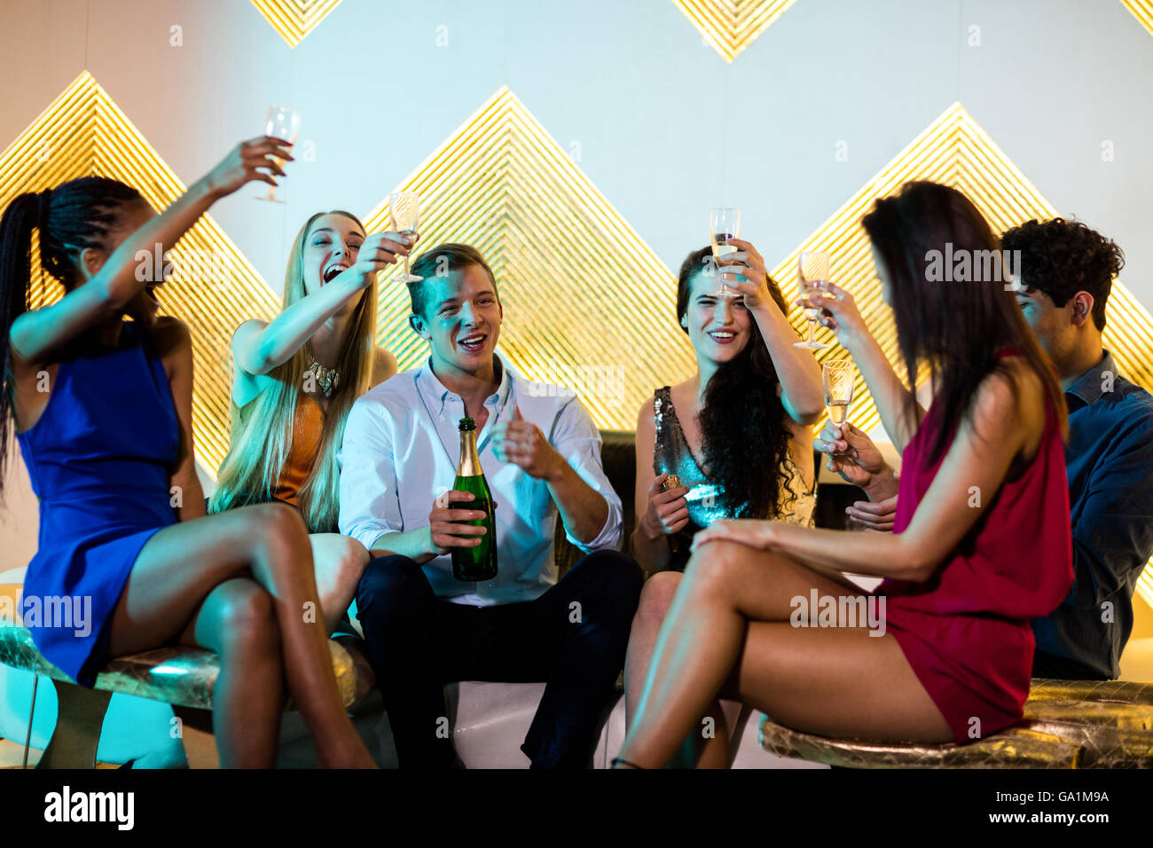 Group of smiling friends sitting on sofa and toasting a glasses of ...