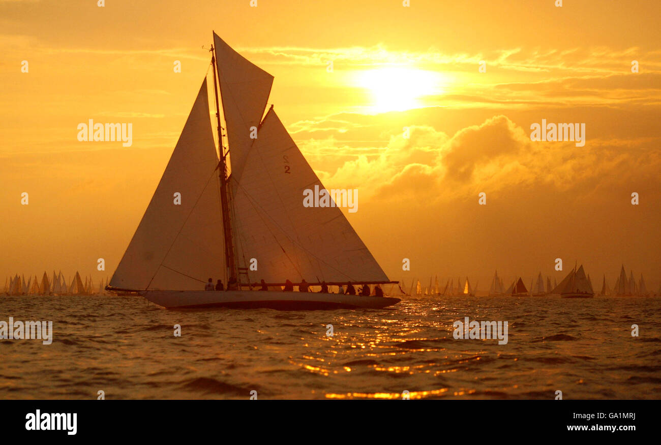 The sun rises as Kelpie, a 1903 Solent One Design gaff races off the start line at Cowes, Isle of Wight, at the beginning of the JP Morgan Round the Island Race. The start was brought forward to 5am after some boats failed to beat the tide last year and got stuck at The Needles. Stock Photo