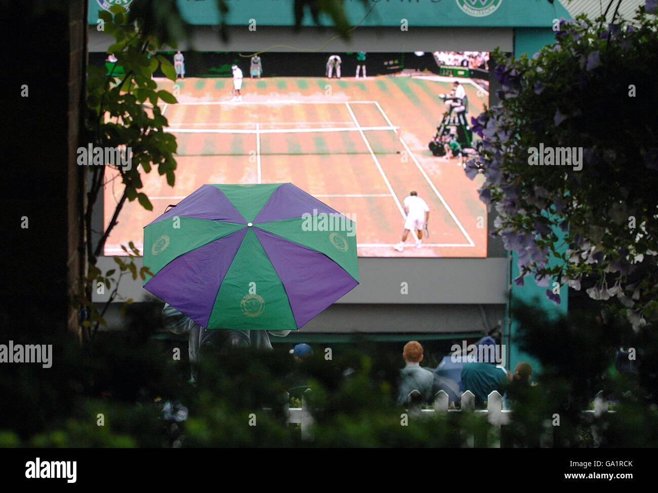 Fans watch the tv screen on Henman Hill as rain delays play during The