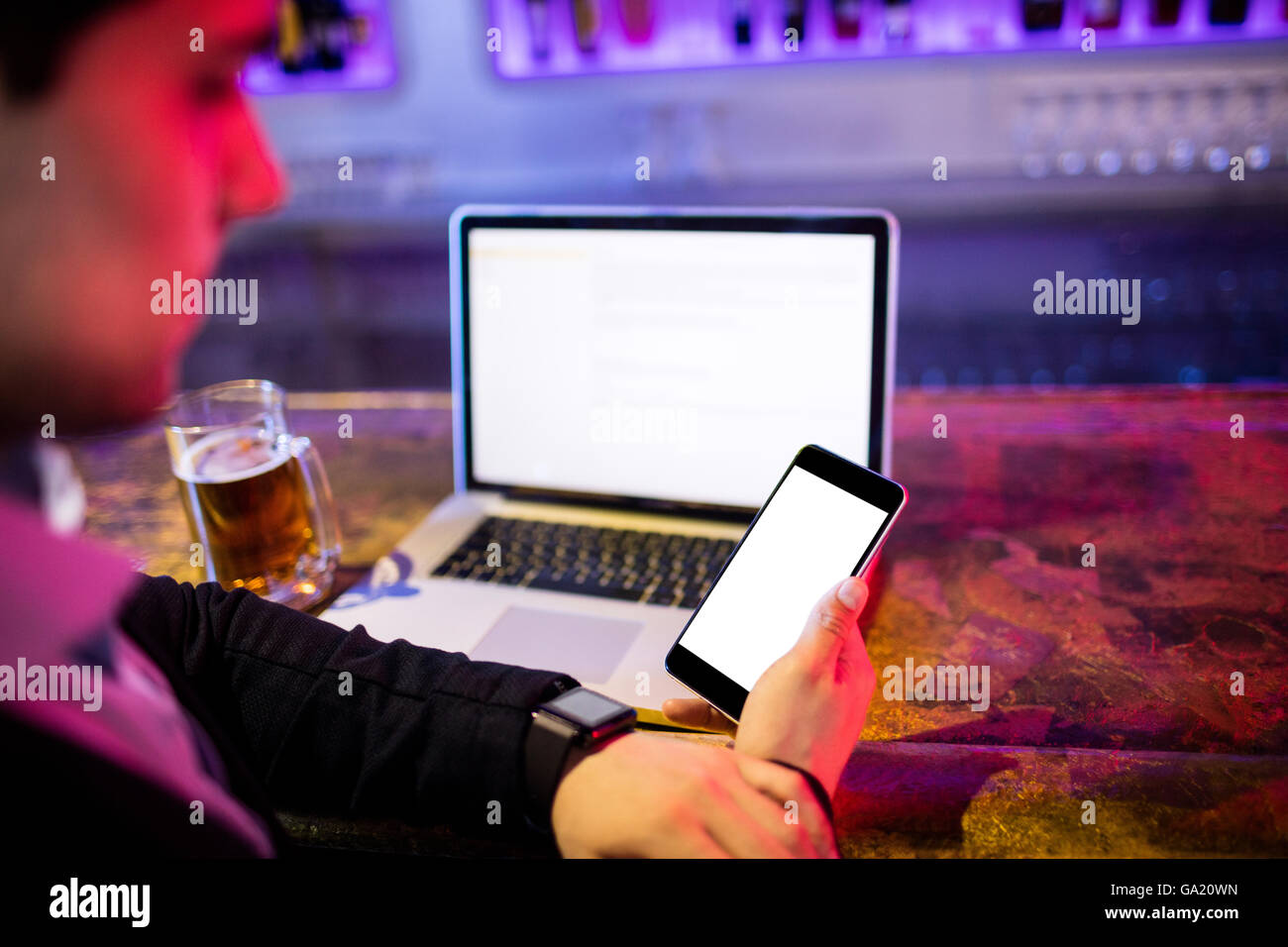 Man using mobile phone with glass of beer and laptop on table at bar counter Stock Photo