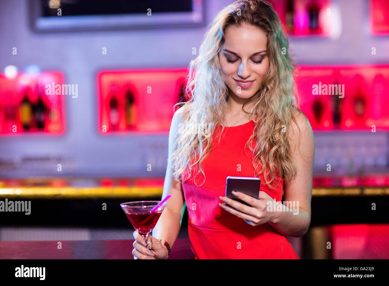 Beautiful woman using mobile phone while having cocktail Stock Photo