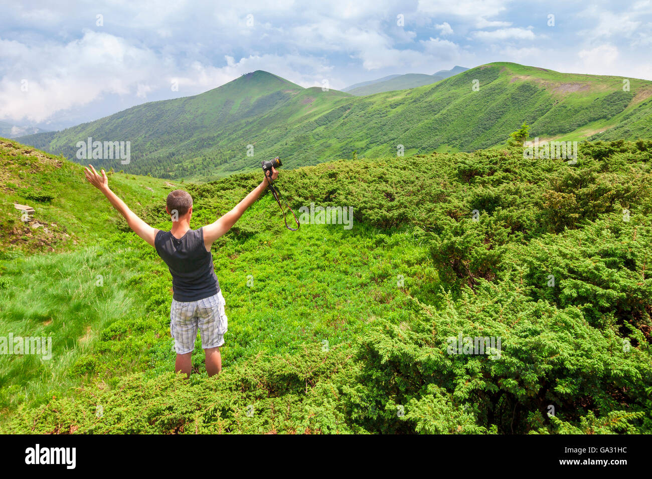Man standing in mountains with camera raising hands Stock Photo