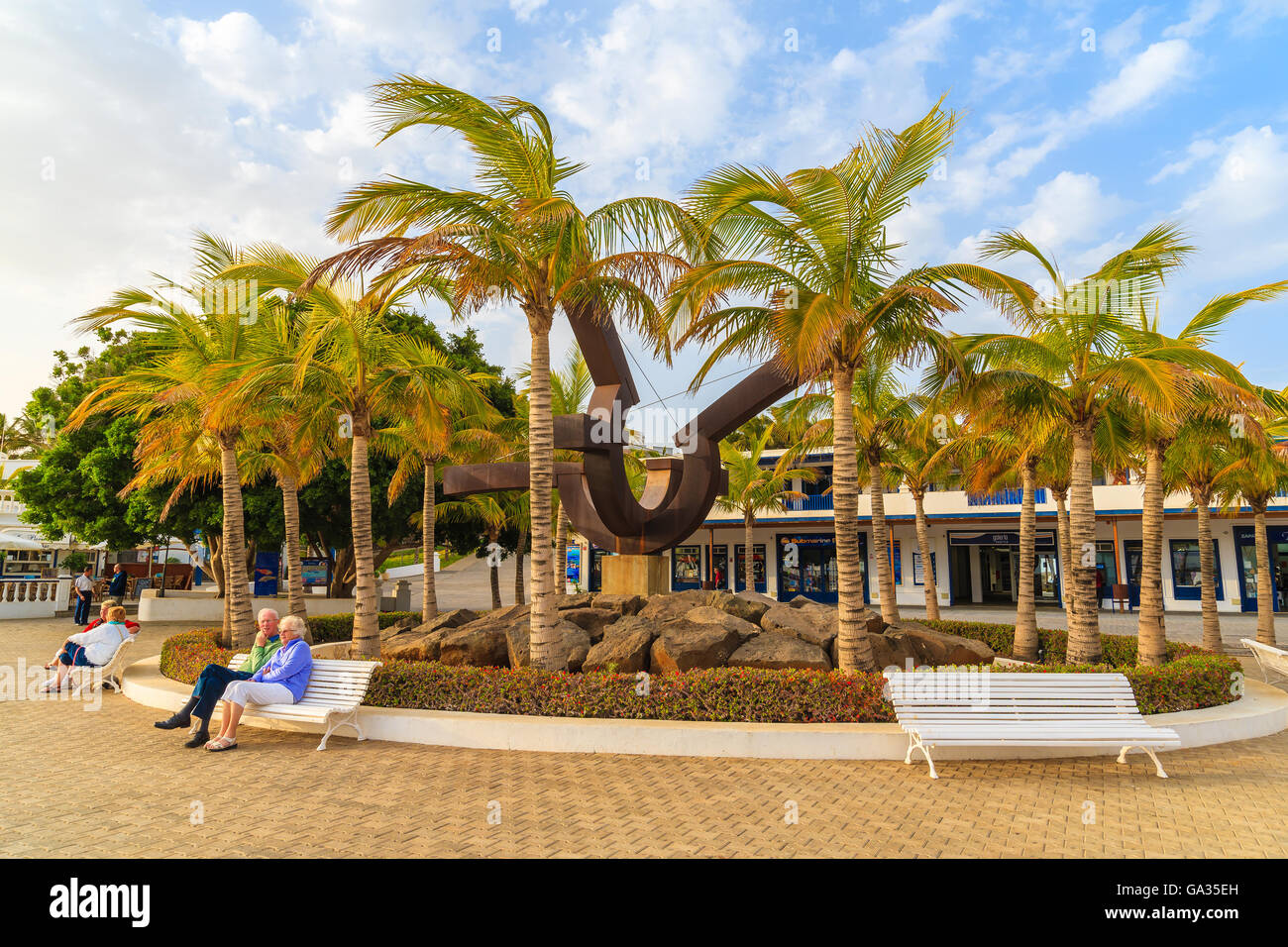 PUERTO CALERO MARINA, LANZAROTE ISLAND - JAN 12, 2015: square with palm trees and people sitting on bench in Puerto Calero port built in Caribbean style. This is a modern yacht marina. Stock Photo