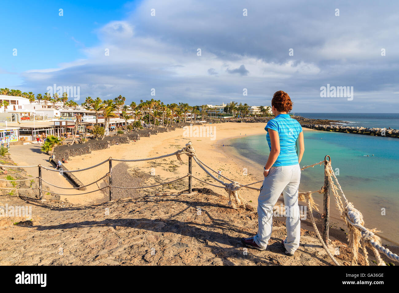 PLAYA BLANCA, LANZAROTE ISLAND - JAN 16, 2015: young woman tourist looking at Flamingo beach from viewpoint. Canary Islands are popular holiday destination for European tourists in winter time. Stock Photo